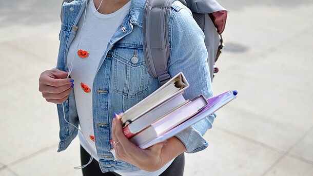 Junge Frau mit Bücherstapel in der Hand und Rucksack